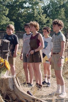 several young people standing in front of a tree stump with sunflowers on it