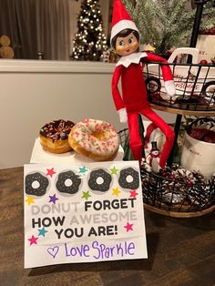 an elf is sitting on a table with doughnuts and a sign that says donut forget how awesome you are