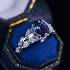 a ring with an oval blue stone surrounded by three pear shaped diamonds in a velvet box