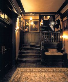 an old fashioned hallway with stairs and pictures on the wall above it's carpet