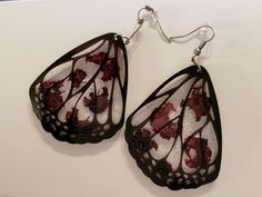 a pair of black and white butterfly wings with red spots on them are hanging from silver earwires