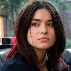 a woman with long hair and red streaks on her face looking off to the side