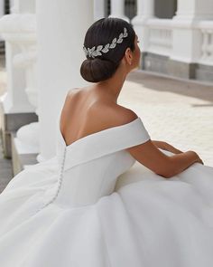 a woman in a white wedding dress sitting on the ground with her back to the camera