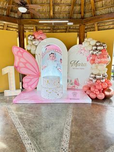 a pink and white cake with a butterfly decoration on the top is surrounded by balloons