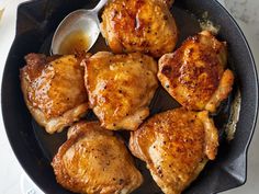 four pieces of chicken in a skillet with a spoon and sauce on the side