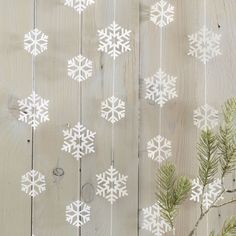 white snowflakes are hanging on a wooden wall next to pine cones and branches