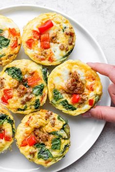 a white plate topped with mini frittatas filled with meat and vegetables next to a person's hand