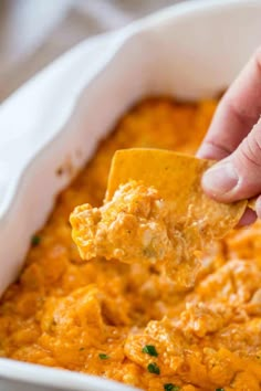 a person dipping a tortilla chip into a casserole dish