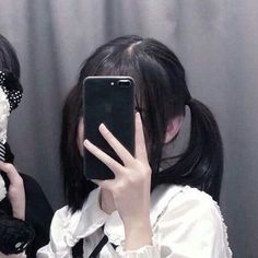 two girls are holding their cell phones up to their faces and one is holding a teddy bear