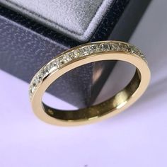 a yellow gold wedding ring with small diamonds on it's side, in front of a black box