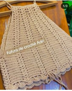 a crocheted apron is sitting on top of a wooden table with the words fofura de crochet alpi