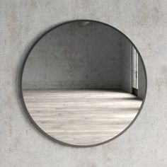 a round mirror hanging on the wall in front of a wooden floor and white walls