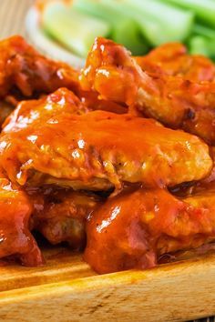 chicken wings covered in marinara sauce on a wooden cutting board with celery