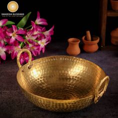 a large golden bowl with handles sitting on a table next to vases and flowers