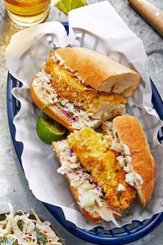 two fish sandwiches with cole slaw and lime on a blue plate next to a glass of beer