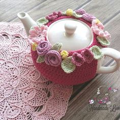 a crocheted tea pot with flowers on it and a doily next to it