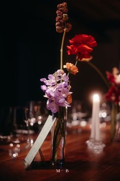 flowers in a vase on a table with candles and wine glasses behind it, as well as a name tag