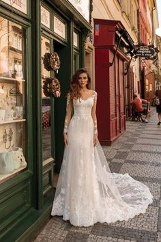 a woman standing in front of a store wearing a wedding dress with long sleeves and an open back