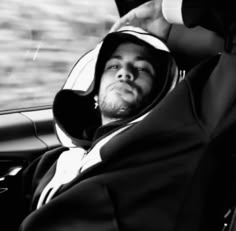 a man sitting in the passenger seat of a car wearing a hoodie and holding his hand up to his head