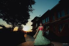 a woman in a green and pink dress is walking down the street at sunset or dawn