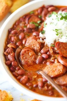 a white bowl filled with red beans and sausage next to bread on a marble counter