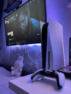 a gaming console with a laptop and monitor on the wall in front of it, next to a teddy bear