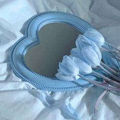 a heart shaped mirror sitting on top of a white bed covered in sheets and flowers