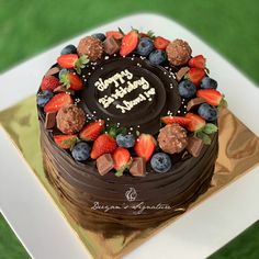 a chocolate birthday cake with strawberries and blueberries on top is sitting on a gold plate