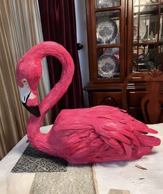 a pink flamingo statue sitting on top of a table next to a china cabinet