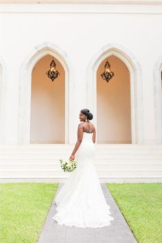 a woman standing in front of a white building holding a bouquet and looking at the camera