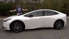 a man standing next to a white car in a parking lot with his hands out