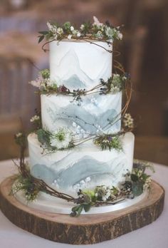 a three tiered wedding cake decorated with greenery and white flowers on a wooden stand