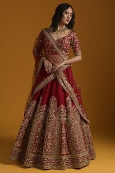 a woman in a red and gold lehenga, standing against a yellow background