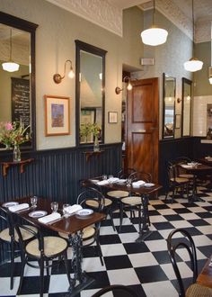 a restaurant with black and white checkered flooring, wooden tables and chairs in the center