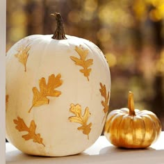 two pumpkins sitting on a window sill with gold leaves painted on the front