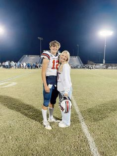 a man and woman standing on top of a football field with lights in the background