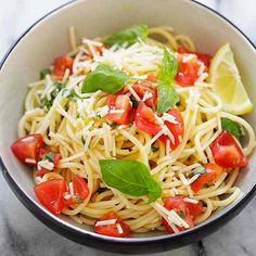 a bowl filled with pasta, tomatoes and spinach on top of a marble table