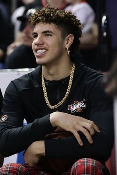 a young man sitting in the stands at a basketball game wearing a black shirt and plaid pants