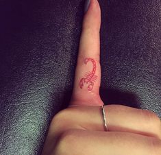 a person's finger with a tattoo on it that has the letter c in red ink