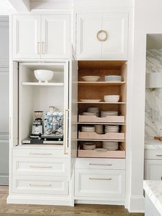 an open cabinet in a kitchen with white cabinets and marble counter tops on both sides