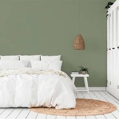 a bedroom with green walls, white bedding and an area rug on the floor