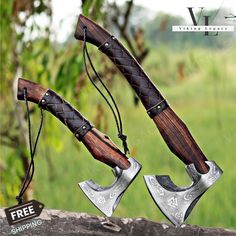 two axes with leather handles are on display in front of a green field and trees