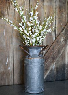 a metal vase with flowers in it sitting on a table next to a wooden wall