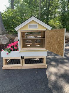 a small chicken coop with flowers in the front and side windows on it's sides