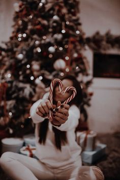 a woman sitting in front of a christmas tree holding a candy cane with both hands