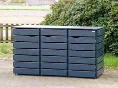 a large blue box sitting on top of a brick sidewalk next to a bush and wooden fence