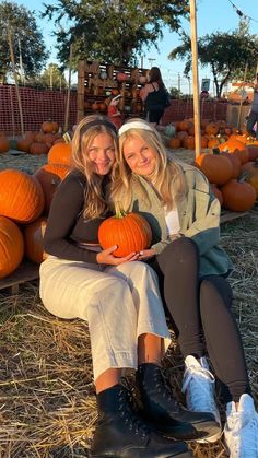 two women sitting on the ground with pumpkins in the background at a pumpkin patch