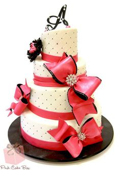 a three tiered cake decorated with pink and black ribbon, bows and monograms