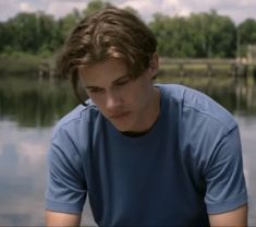 a young man is sitting by the water