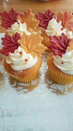 four cupcakes with frosting and leaves on them are sitting on a table